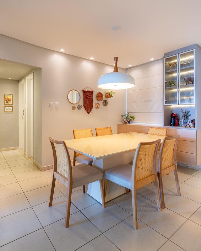 A sala de jantar na planta desse apartamento é um ambiente central que conecta todos os outros da casa. Ela está diretamente ligada à cozinha, à sala de estar e também à área de circulação, que leva para os quartos. Em alguns lares, a sala de jantar é pouco utilizada, mas aqui não foi o caso. Essa mesa acomoda a família para as refeições diárias, além de ser ponto de encontro para ajudar na lição de casa das crianças, jogos em família, um espaço verdadeiramente multiuso! Por isso a ideia foi trazer leveza, descontração e muita funcionalidade para esse cômodo! Reparem também no detalhe da circulação cheia de estilo! ???? A textura em cimento queimado e a iluminação pontual nos quadros proporcionaram um sensação de intimidade que o ambiente já sugere.